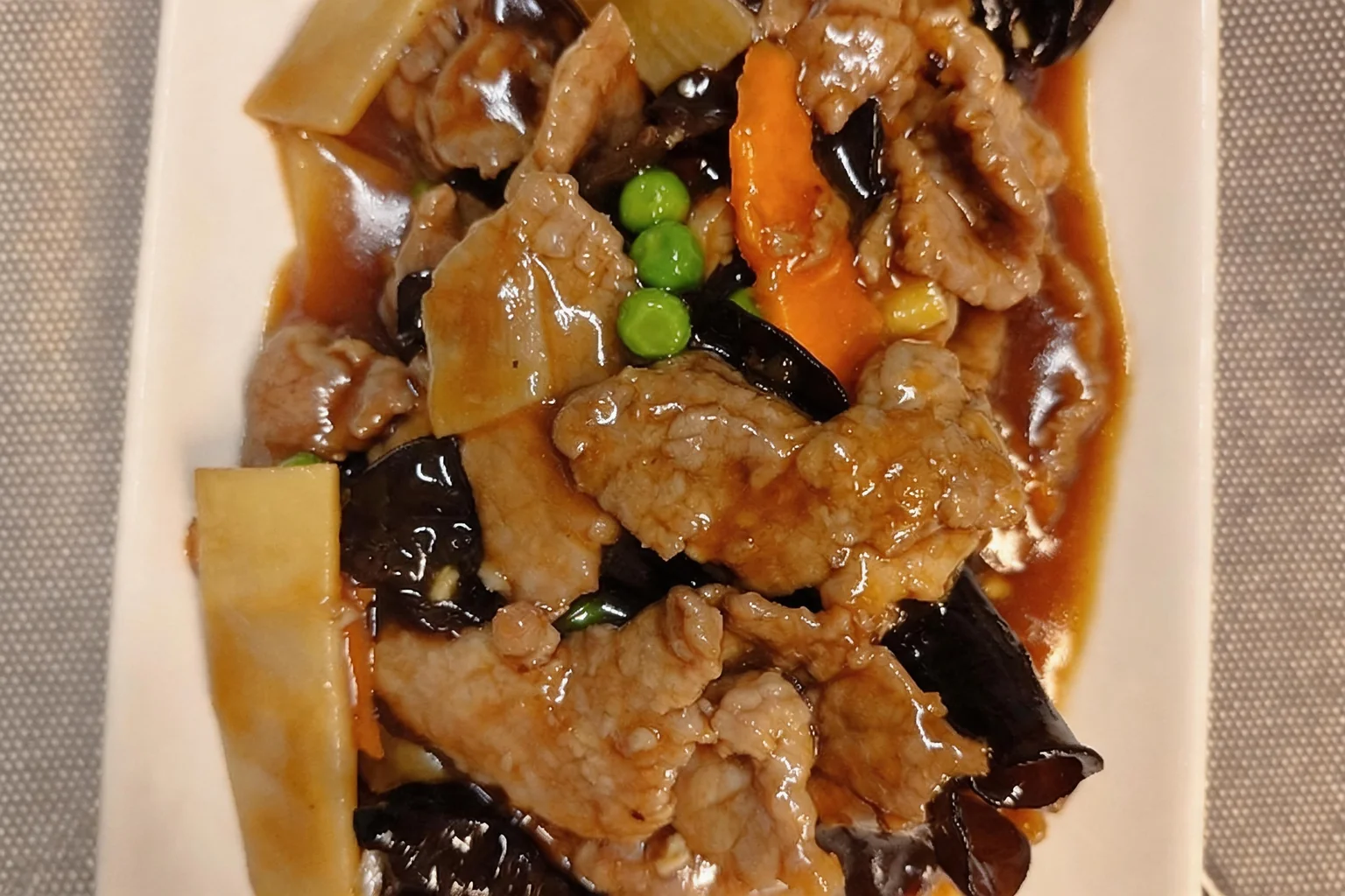 54 Beef stir-fried with black mushrooms, white rectangular plate, grey placemat