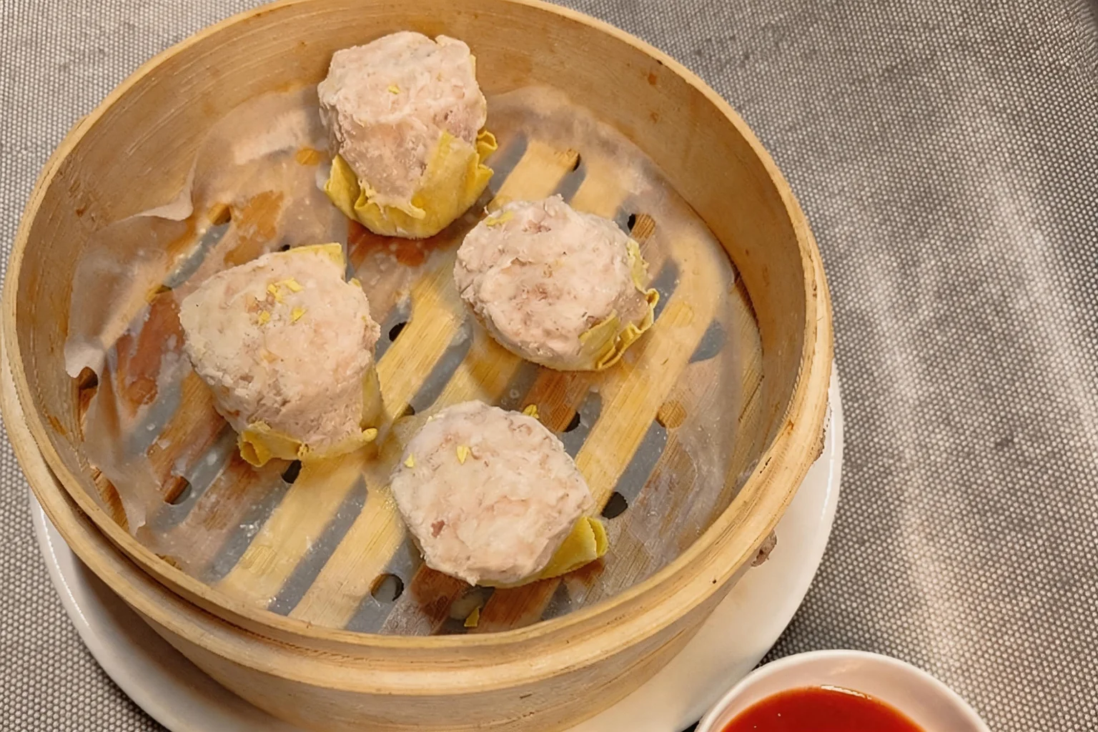 V5 Prawn dumplings in a bamboo basket, small dish of red sauce, grey placemat